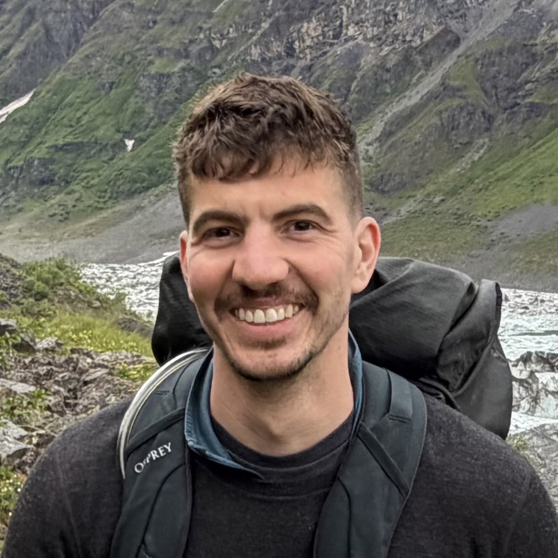 Christopher smiling beside a wide Alaskan landscape